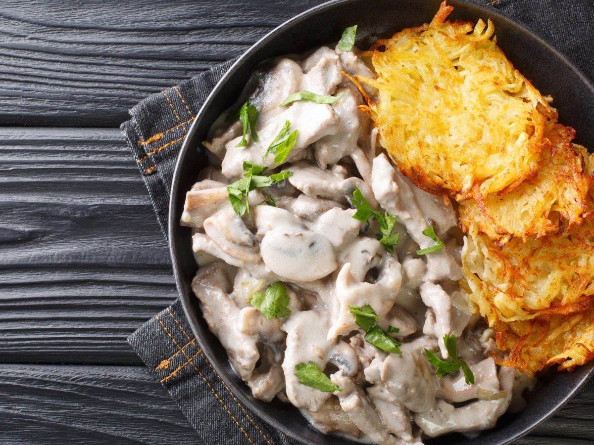 Zürcher Geschnetzeltes mit Rösti auf schwarzem Teller.