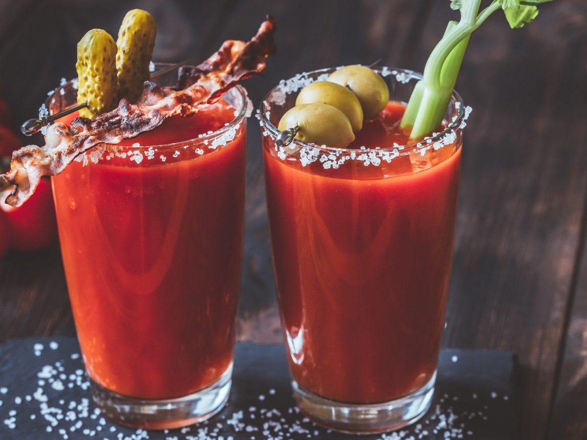 Bloody Mary: Longdrink mit Tomate, Wodka, Tabasco und Worcestersauce garniert mit Bacen, Oliven, Sellerie und saurer Gurke auf einem Holzbrett