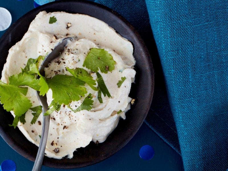 Frischkäse Dip mit Sesamcreme garniert mit frischem Koreander in einer schwarzen Schale auf blauem Tuch serviert