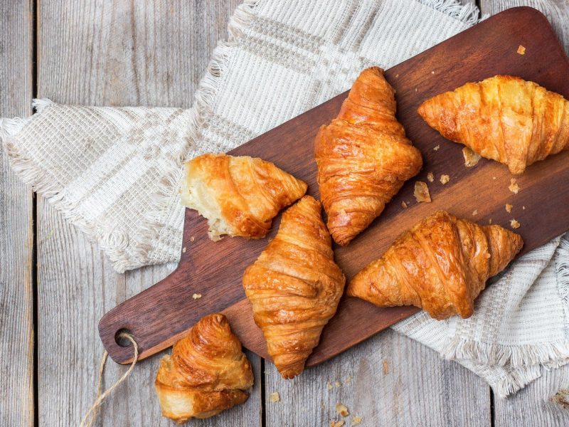 In der Draufsicht sieht man Kartoffelcroissants auf einem Holzbrett liegen, das Brett liegt auf weißem Holz.