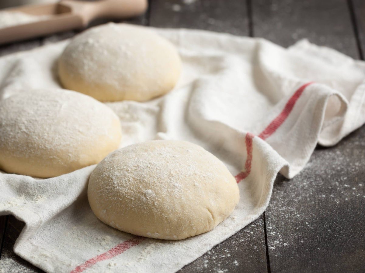 Germknödel mit Mehl ummantelt auf einem weißen Tuch auf hölzerner Arbeitsfläche