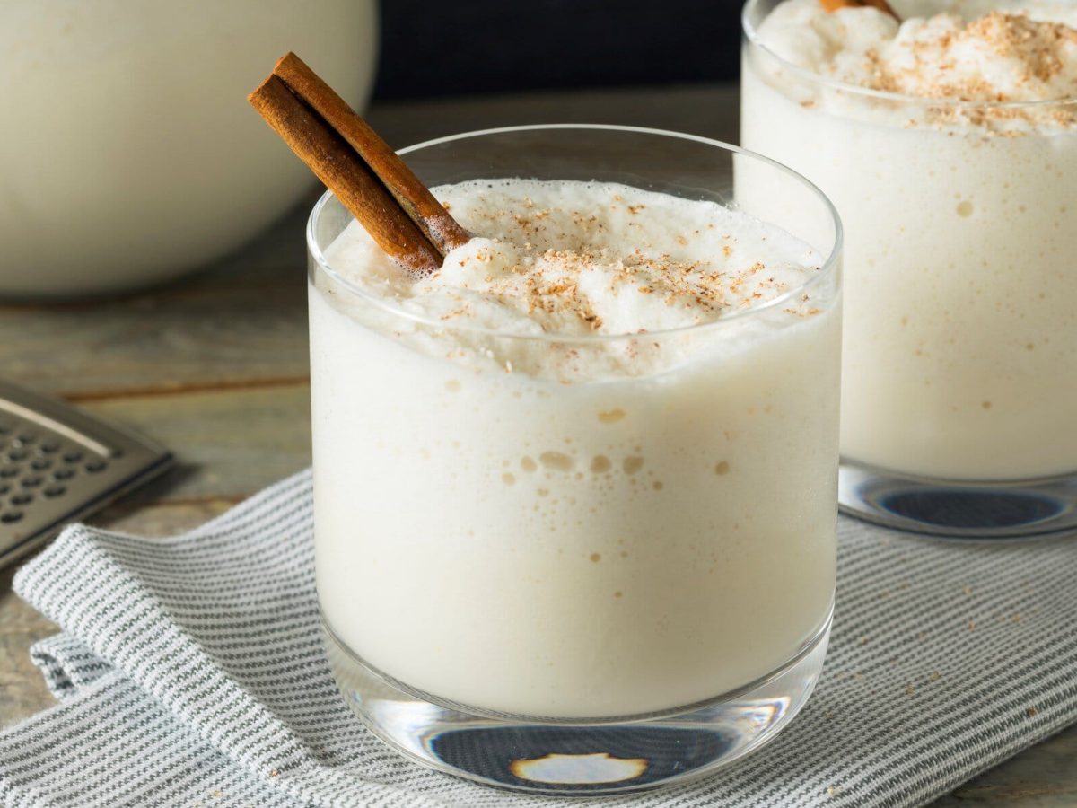 Zwei Gläser mit heißer Milch und Whiskey, dekoriert mit Zimtstangen.