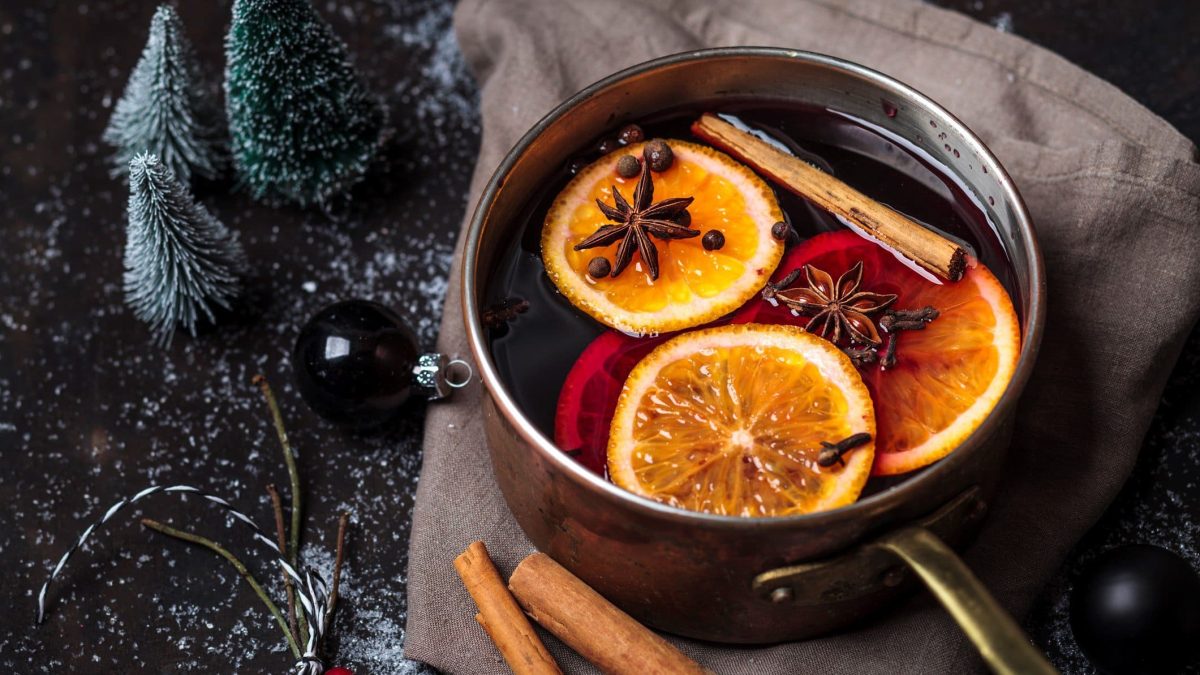 Selbst gemachtes Glühweingewürz: Ein Topf mit Glühwein, Orangen, Zimt und Anis steht auf dunklem Untergrund, daneben kleine Deko-Bäume und Kugeln.