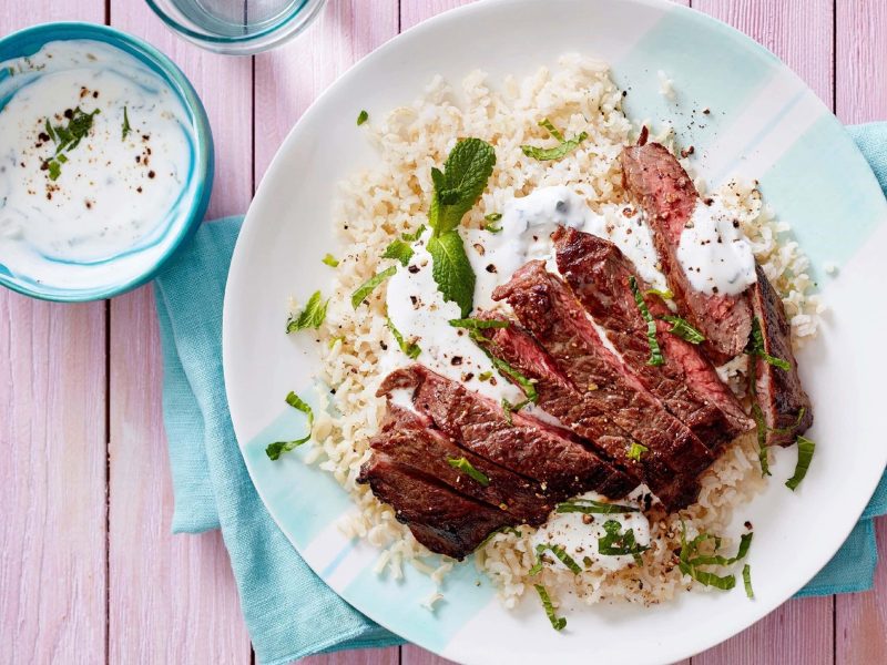 Steak in streifen geschnitten mit Joghurt-Minzsoße auf Reis, auf einem weißen Teller mit blauen Servietten serviert