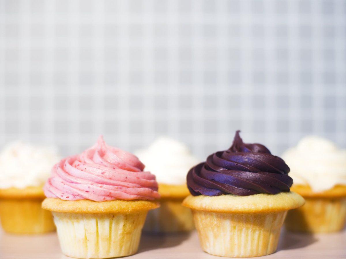 Fünf Cupcakes mit bunten Creme-Hauben stehen vor einem hellen Hintergrund.