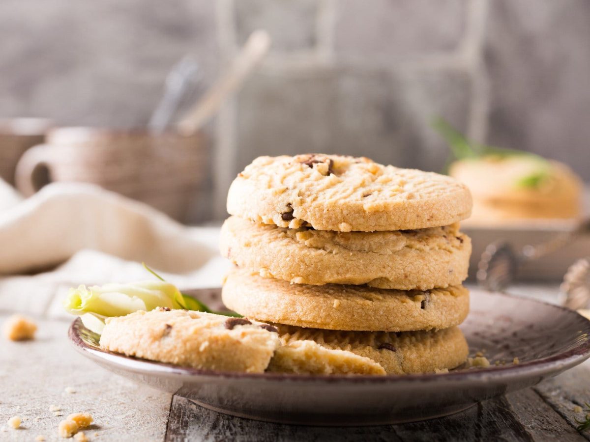 Ein Teller mit einem Stapel veganer Orangen-Schoko-Plätzchen, dahinter ist unscharf Küchenausstattung zu erkennen.