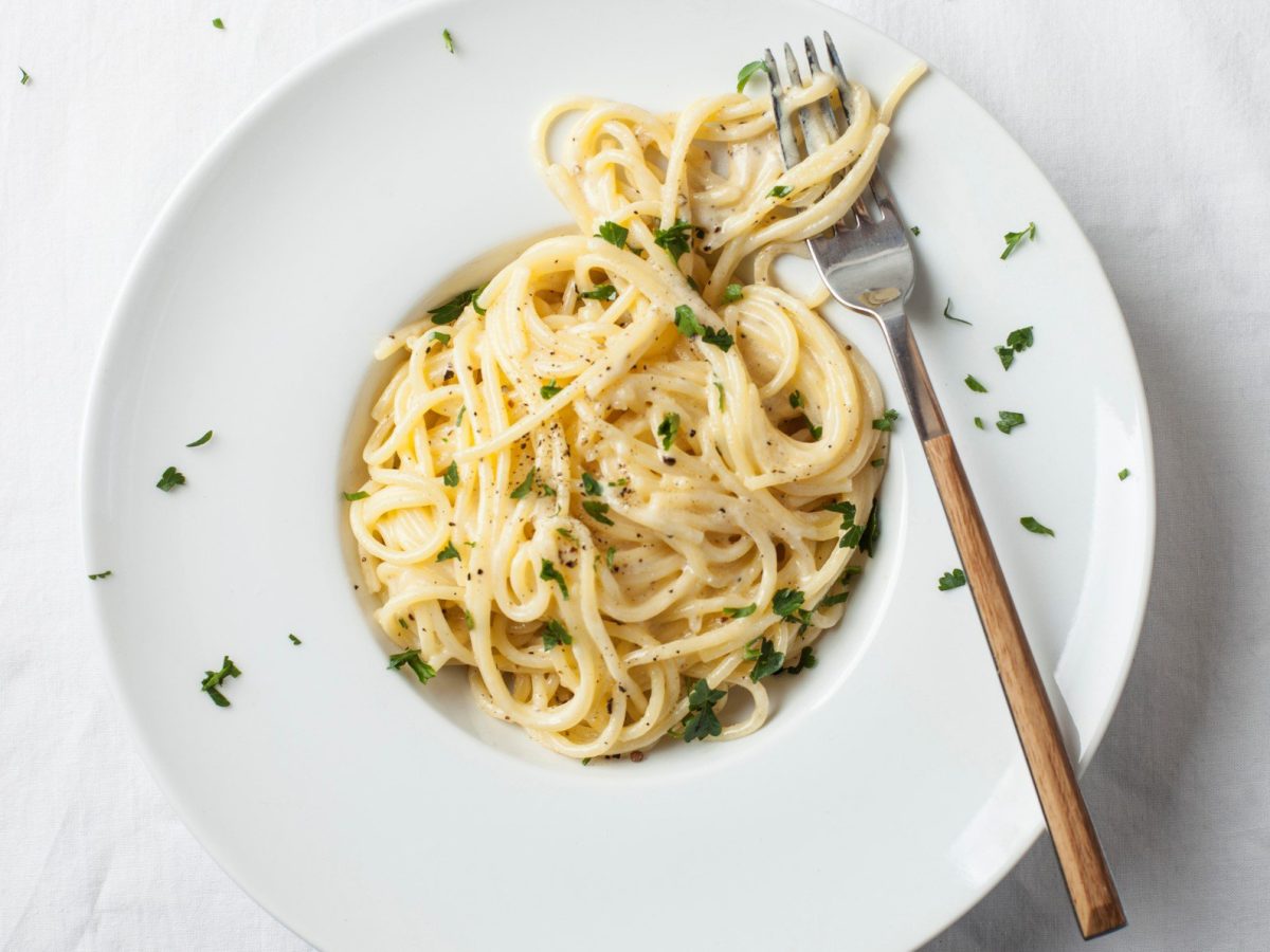 Ein Teller mit veganen Spaghetti Alfredo in der Draufsicht, darauf liegt eine Gabel.