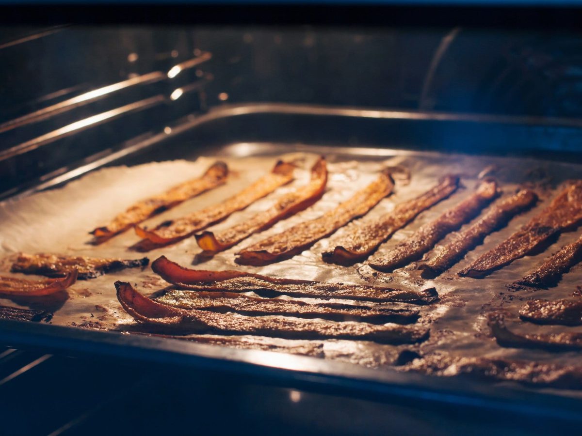 Mehrere Scheiben veganer Bacon liegen auf einem mit Backpapier ausgelegtem Backblech.