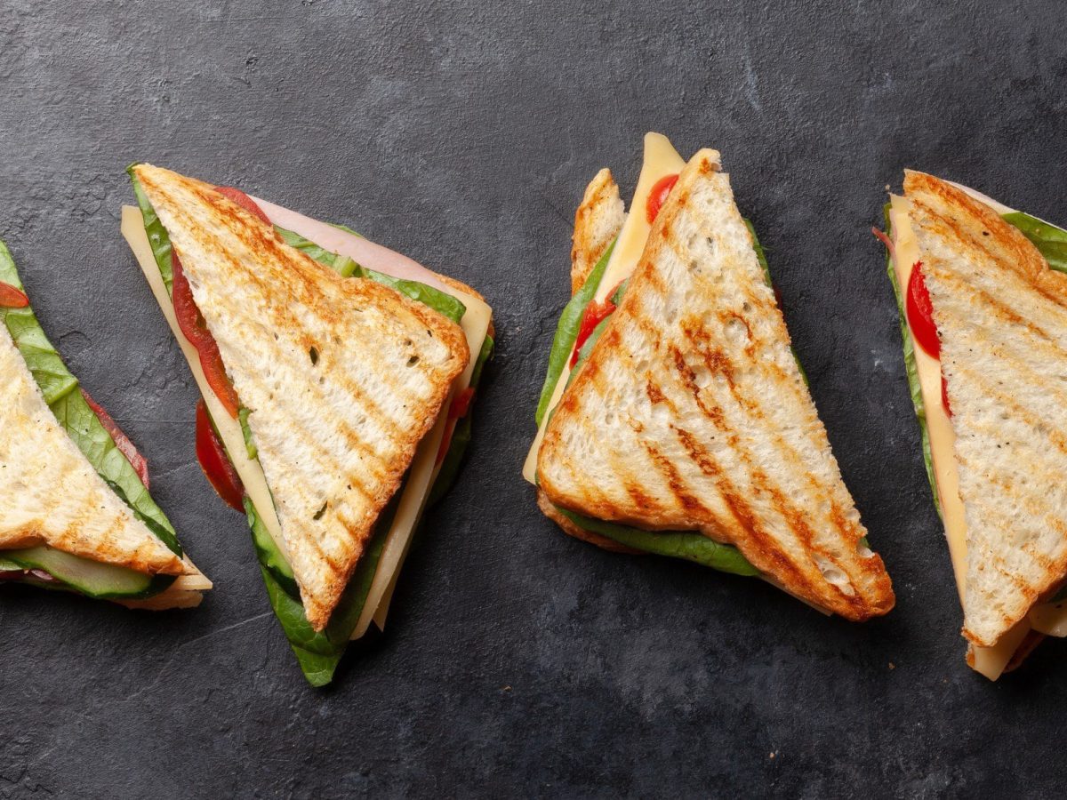 Mehrere Club-Sandwichs mit Schinken, Käse und Salat auf Schiefer-Platte