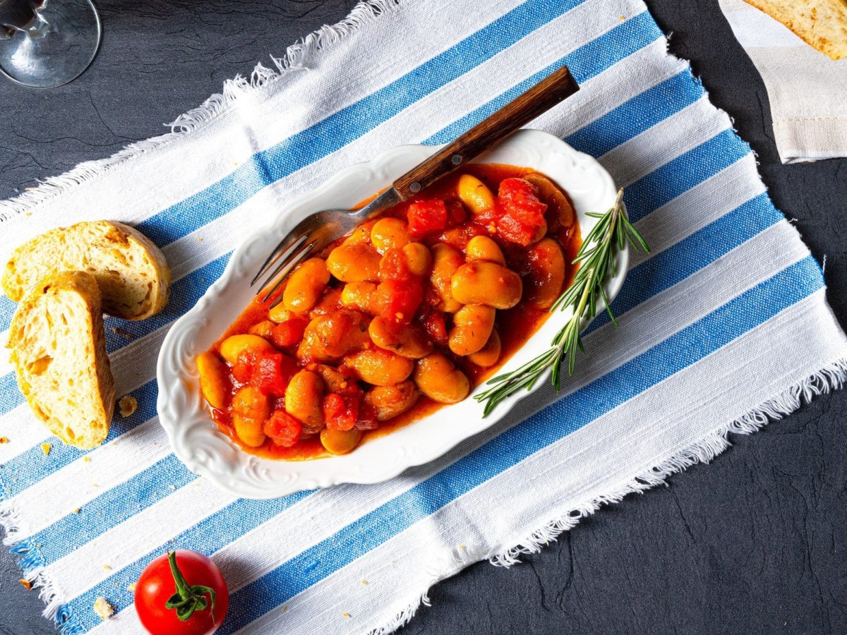 Weißer Teller mit griechischen Bohnen in Tomatensauce. Es handelt sich um Gigantes Plaki.