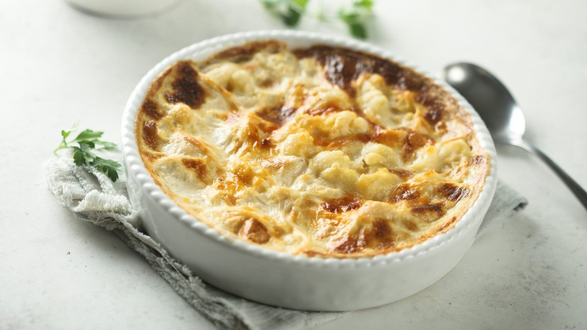 Gnocchi-Gratin mit Blumenkohl und Schinken auf hellem Untergrund.