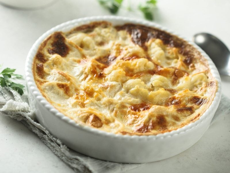 Gnocchi-Gratin mit Blumenkohl und Schinken auf hellem Untergrund.