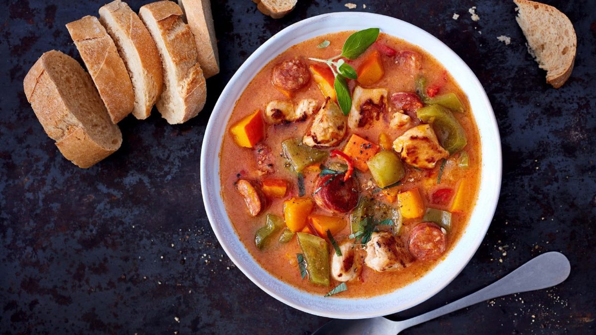 Kürbis-Gulasch mit Huhn, Chorizo, Paprika in Tomatensauce in hellem tiefen Teller serviert mit frischem Brot auf dunklem Hintergrund