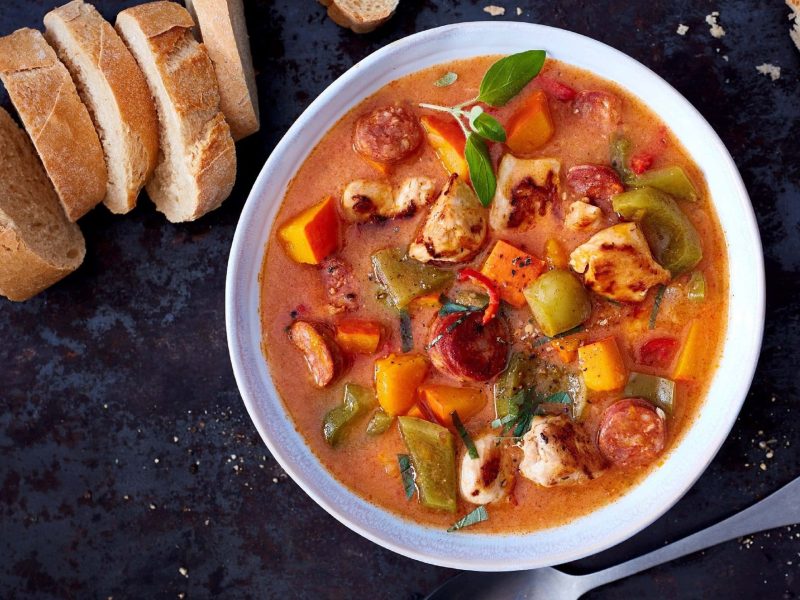 Kürbis-Gulasch mit Huhn, Chorizo, Paprika in Tomatensauce in hellem tiefen Teller serviert mit frischem Brot auf dunklem Hintergrund