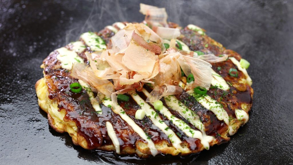 Okonomiyaki mit Bonito-Flocken auf heißer Eisenplatte