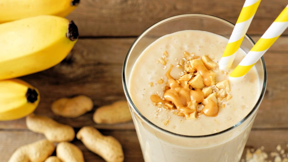 Peanutbutter-Banana-Smoothie in Glas mit zwei Strohhalmen.