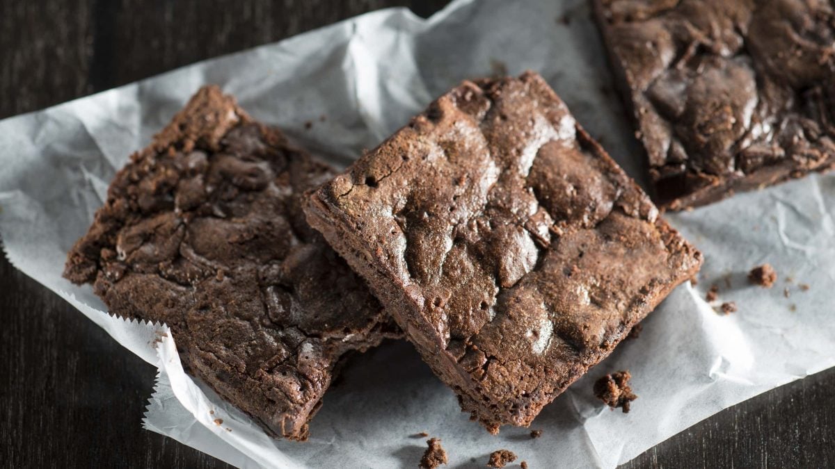 Saftige Brownies mit Sojasauce in Würfel geschinitten und aufeinander gestapelt auf weißem Backpapier auf dunklem Hintergrund