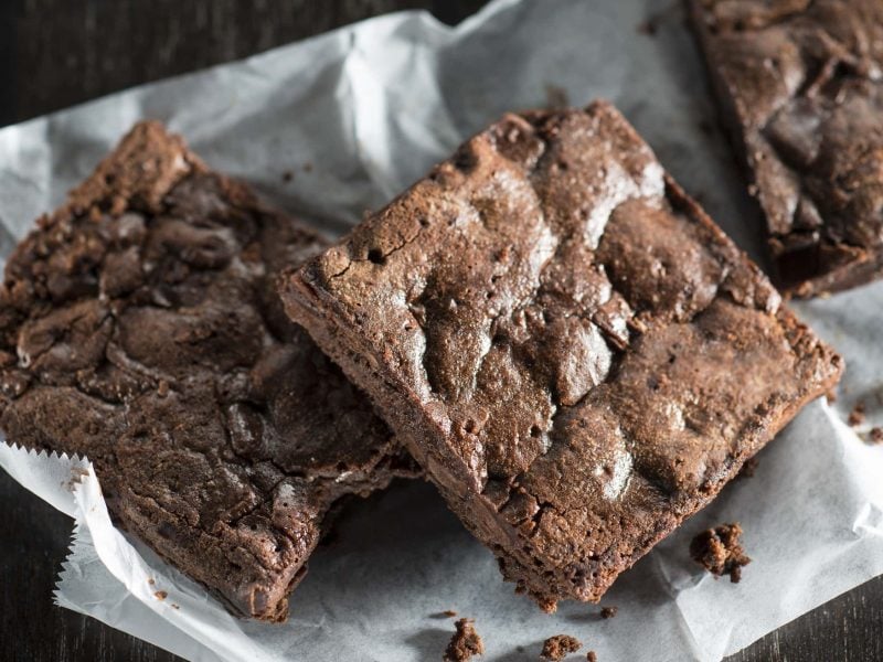 Saftige Brownies mit Sojasauce in Würfel geschinitten und aufeinander gestapelt auf weißem Backpapier auf dunklem Hintergrund