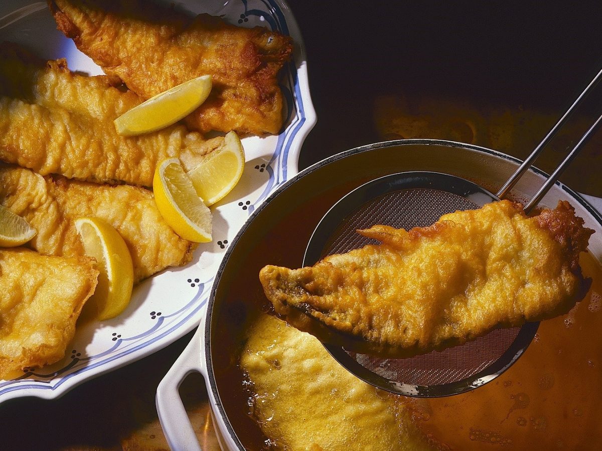 Frittierter Karpfen, aus dem Öl mit einer Schöpfkelle heraus gehoben und in einer Schale zum Abtropfen beiseite gestellt, garniert mit frischen Zitronenscheiben.