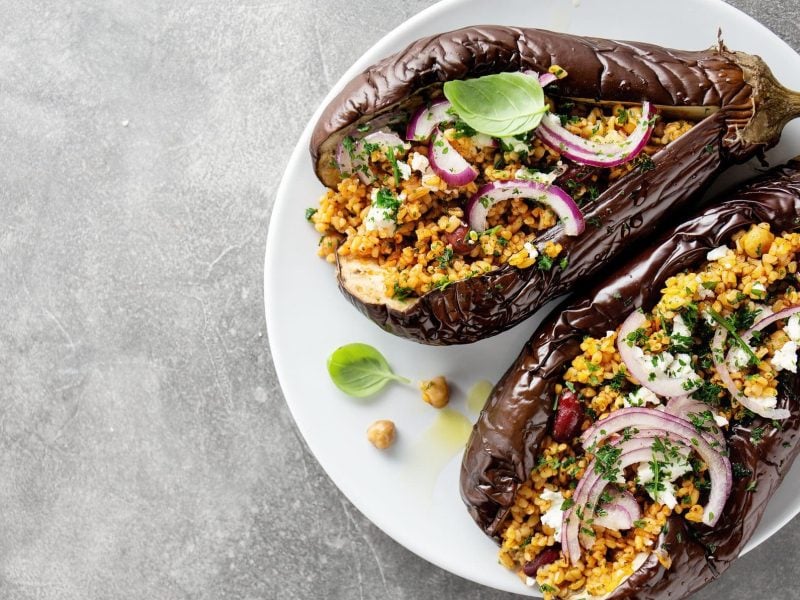 Ein Teller mit gebackener Aubergine mit Bulgur, roten Zwiebeln und Kichererbsen.