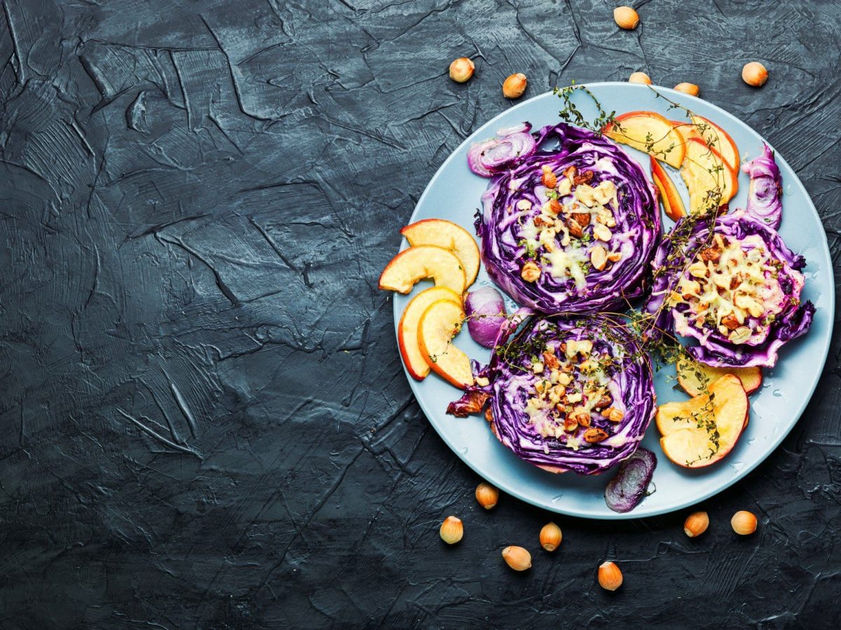 gebackener Rotkohl mit Sesamsauce und Äpfeln auf dunklem Untergrund in der Draufsicht.