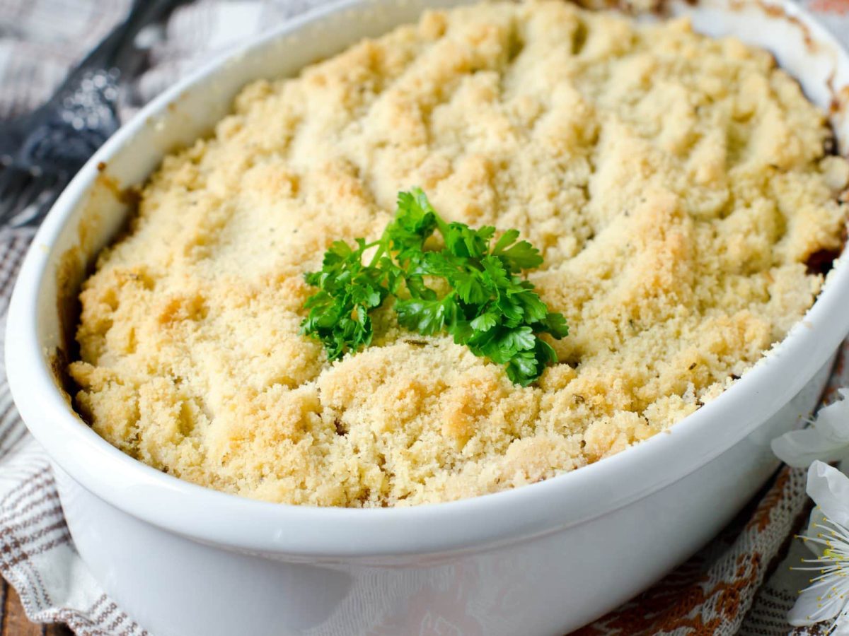 Eine weiße Auflaufform Gemüse-Crumble mit frischen Kräutern dekoriert.