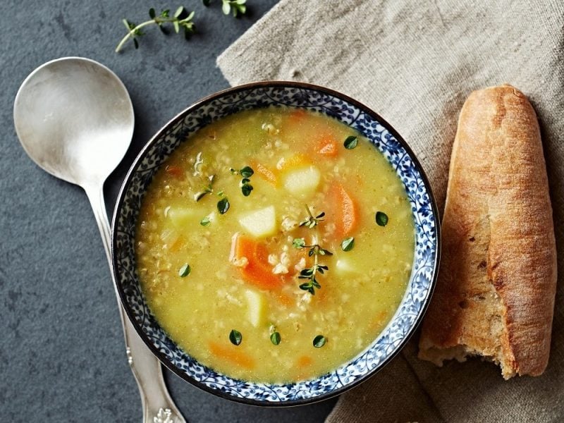 Graupen-Suppe mit Petersilienwurzel, Sellerie, Karotte und Graupen, mit Majoran garniert in einer gemusterten Schale auf einem steinernen Untergrund