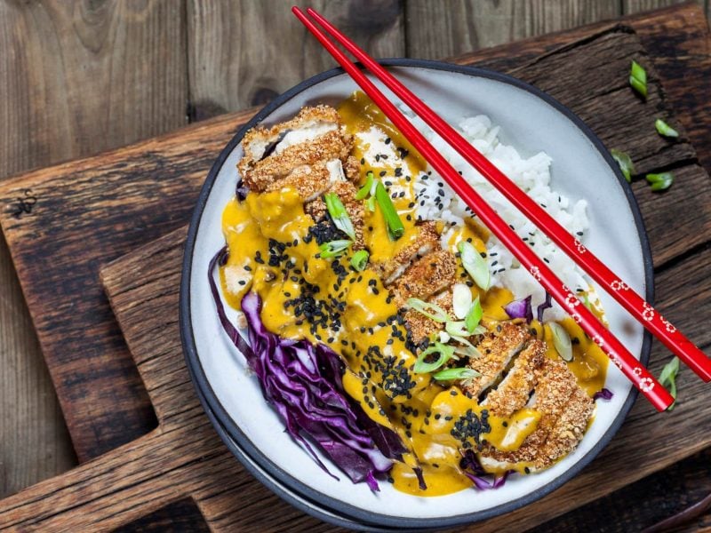 Katsu Curry japansiches Curry Gericht mit Reis und Rotkohl auf weißem Teller, Holzbrettern und Holztisch. Zwei rote Essstäbchen lieben auf dem Teller. Aufnahme aus der Vogelperspektiv.