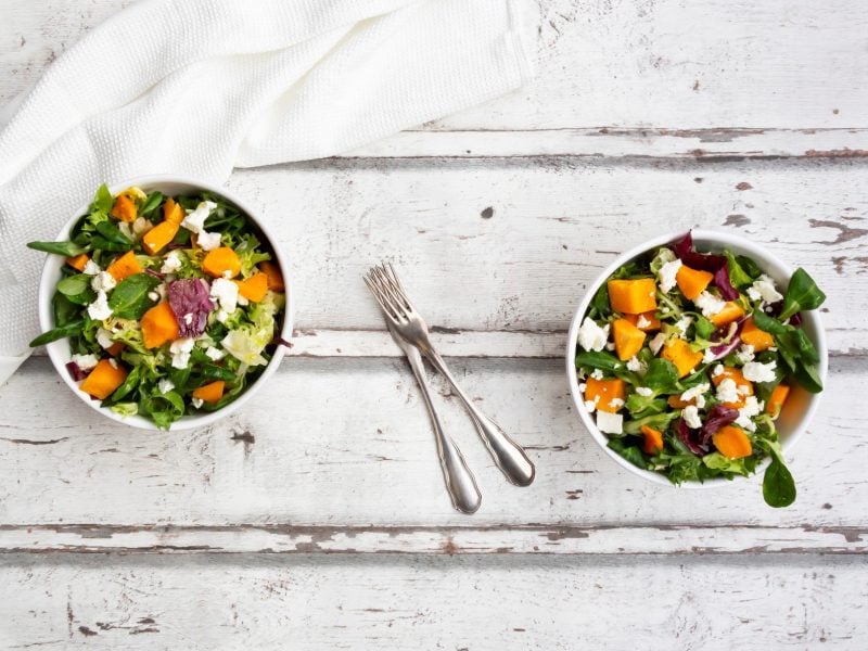 Zwei Schüsseln lauwarmer Salat mit Ofengemüse auf hellem Holz in der Draufsicht.