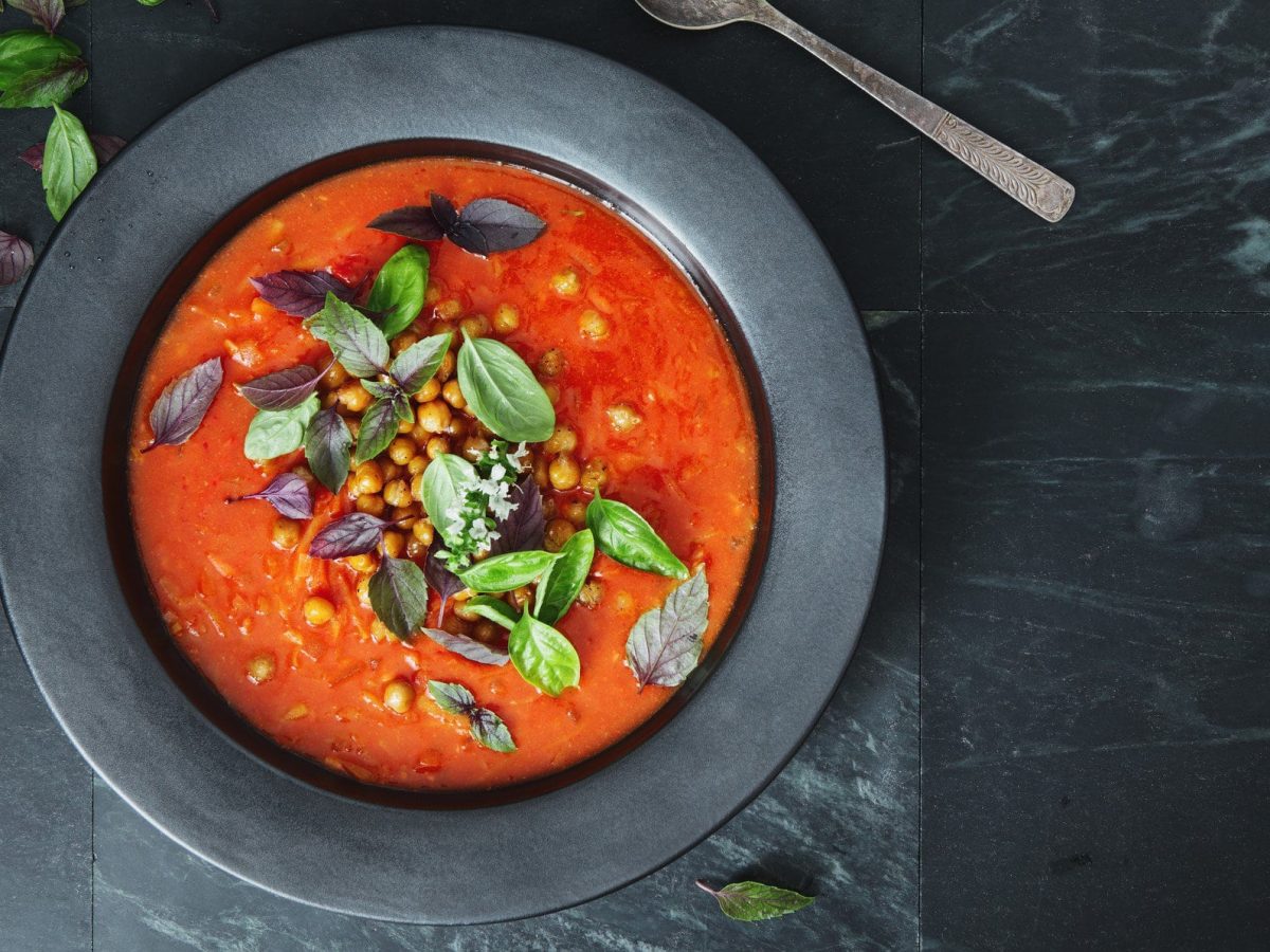 Ein Teller orientalische Tomatensuppe mit Kichererbsen sowie frischen Kräutern in der Draufsicht.