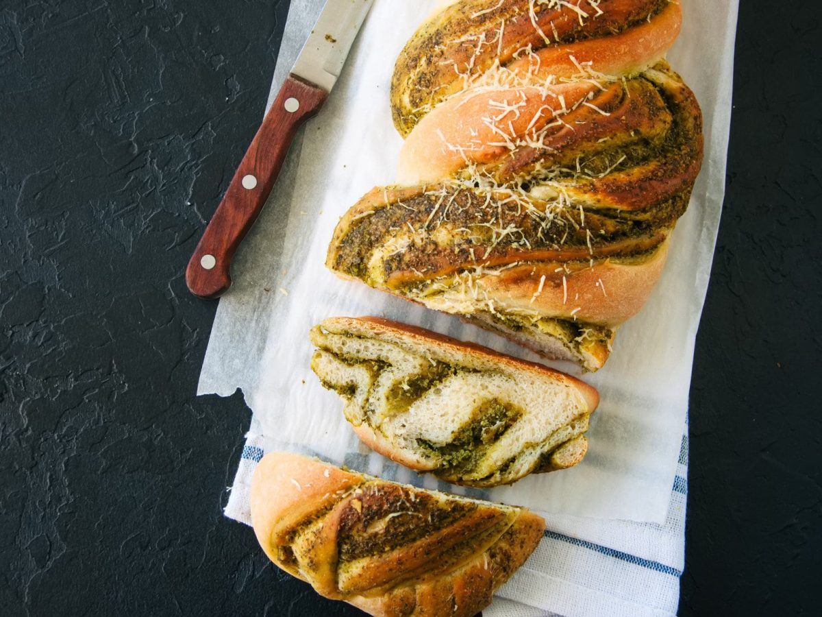 Ein angeschnittenes Pestobrot mit Quinoa in der Draufsicht. daneben liegt ein Messer.