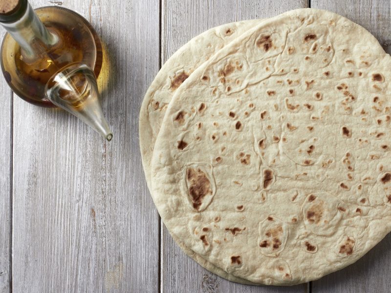 Piadina zwei Piadine Romagnola auf Holztisch. Daneben Olivenöl in einer Glaskaraffe. Aufnahme aus der Vogelperspektive.