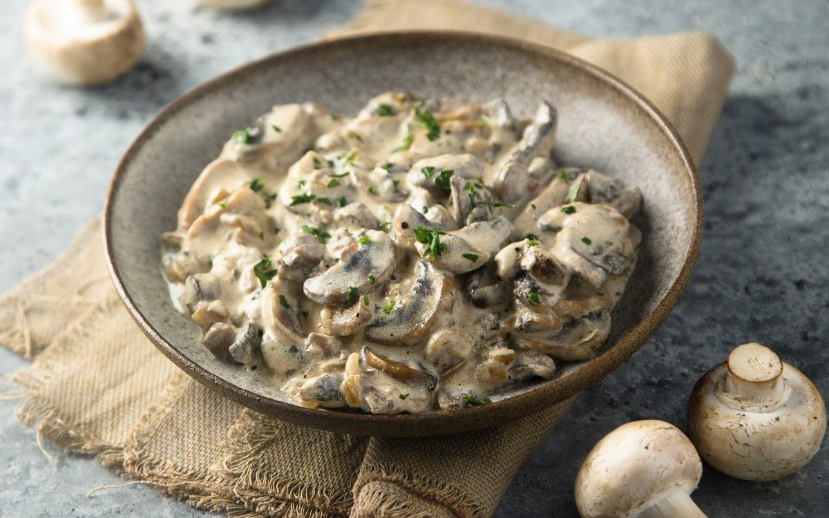 Pilz-Stroganoff: Pilzragout mit Senf, Weißwein und Creme Fraiche in veganer Variante in einer Tonschale, garniert mit frischer Petersilie