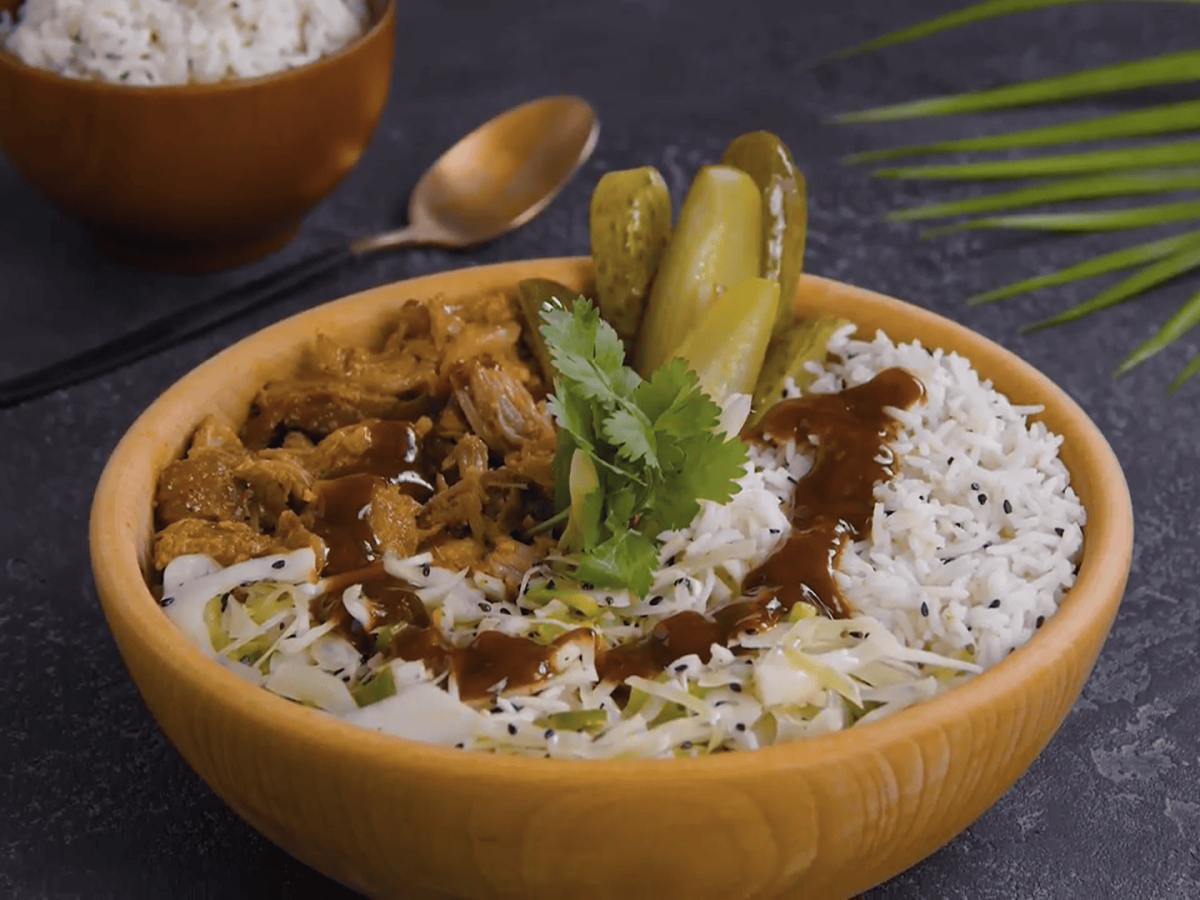 Pulled Pork Bowl mit Koriander und Barbecue-Sauce als Deko in Holzschale auf dunkelgrauem Tisch. Aufnahme aus der Draufsicht.