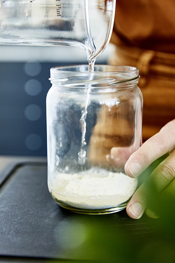 Eine Frau gießt Wasser in ein Glas mit etwas Mehl.