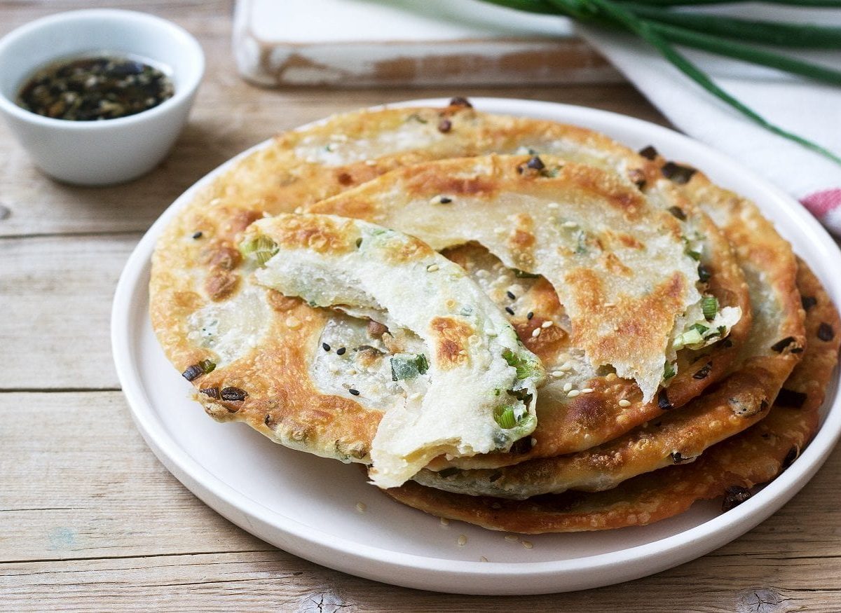 Mehrere Scallion Pancakes liegen auf einem weißen Teller und warten darauf, verzehrt zu werden.