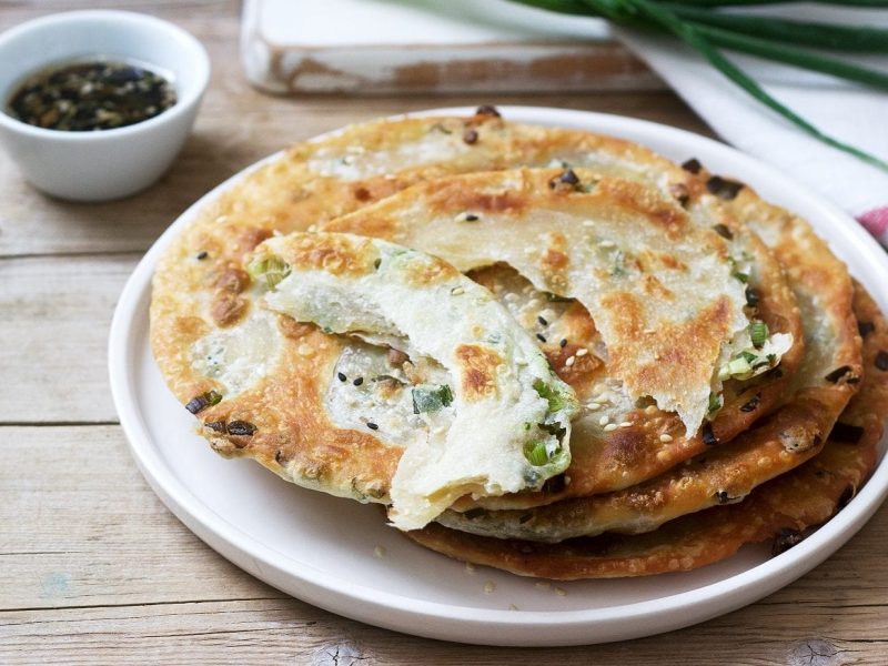 Mehrere Scallion Pancakes liegen auf einem weißen Teller und warten darauf, verzehrt zu werden.