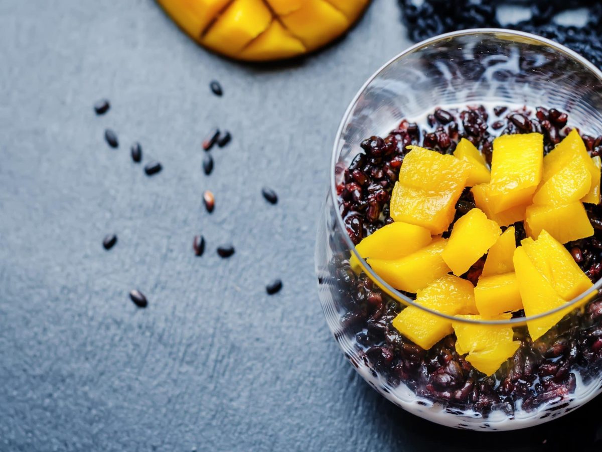 Cremiger Reispudding mit Kokosmilch und gehackter Mango in einem Glas Serviert auf grauem Hintergrund