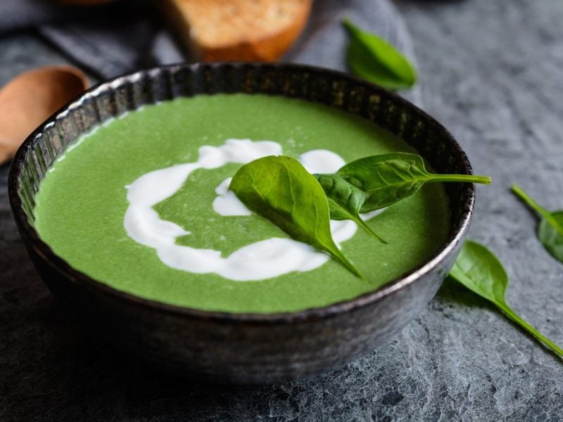 Eine Schüssel mit grüner Suppe und selbst gemachter Hafersahne sowie ein paar Basilikumblättern.