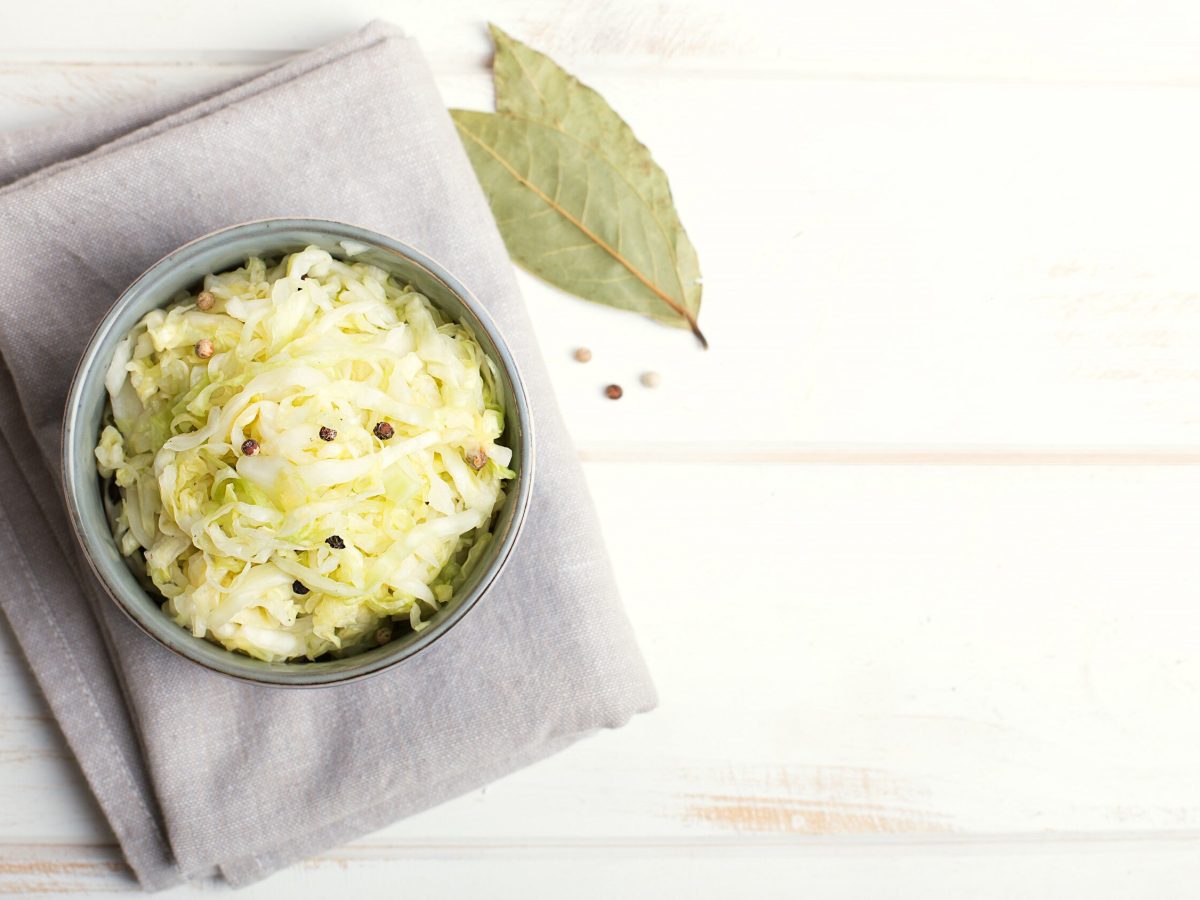 Saftiges selbst gemachtes Sauerkraut gewürzt mit Wachholderbeeren und Lorbeer, serviert in einer Schüssel auf hellem Hintergrund