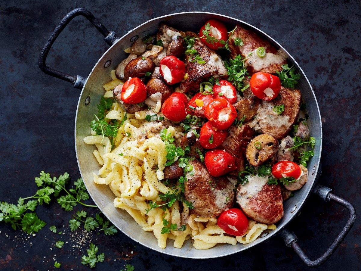 Schweinefilet, Champignons, mit Frischkäse gefüllte Kirschpaprika und natürlich Spätzle: unsere Spätzle-Jägerpfanne steht angerichtet auf einer schwarzen Platte.