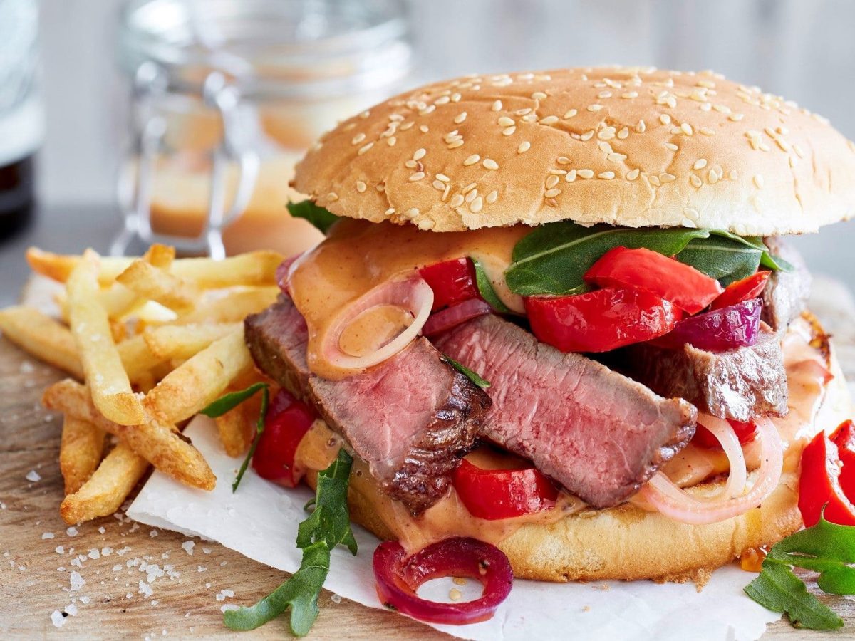 Unser Steakburger angerichtet mit Pommes Frites auf einem Holzbrett.