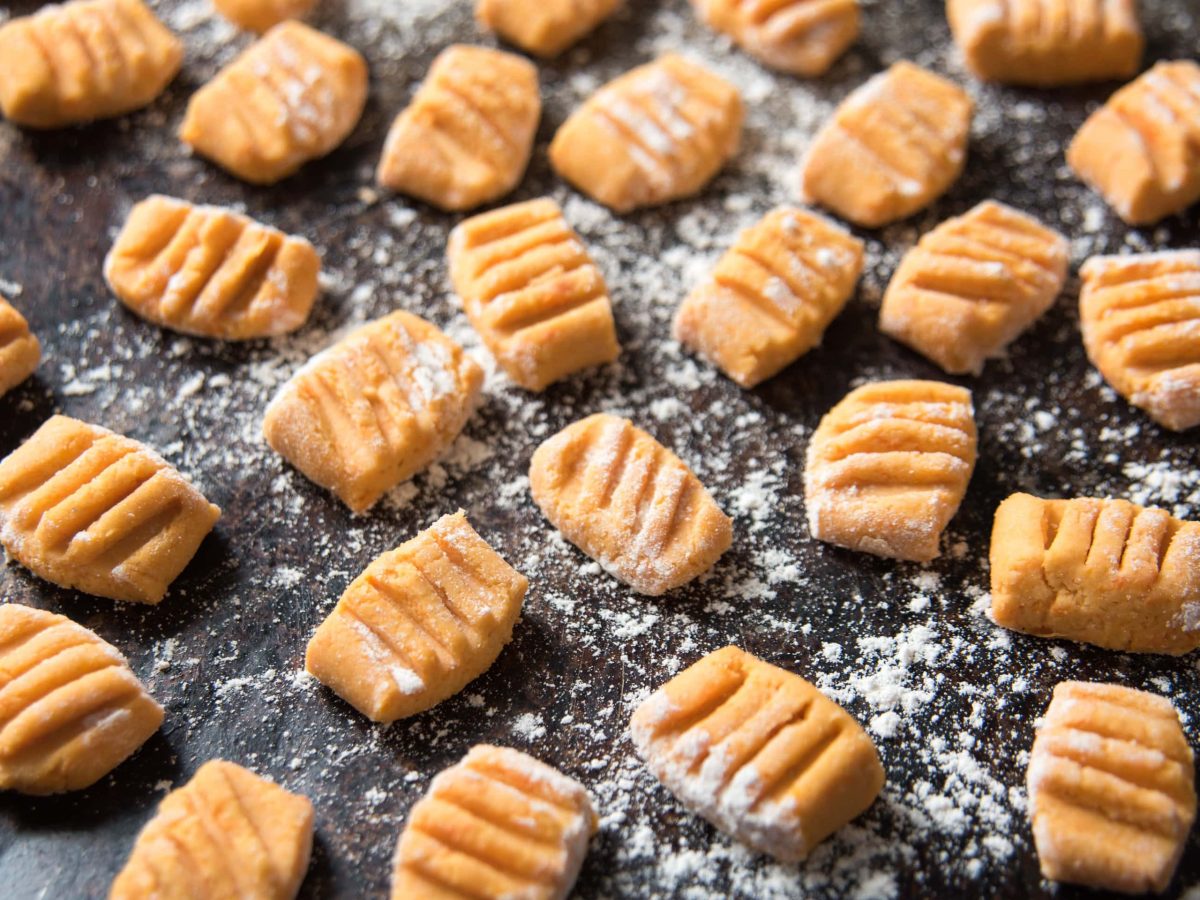 Süßkartoffel-Gnocchi mit Meh auf dunklem Untergrund.