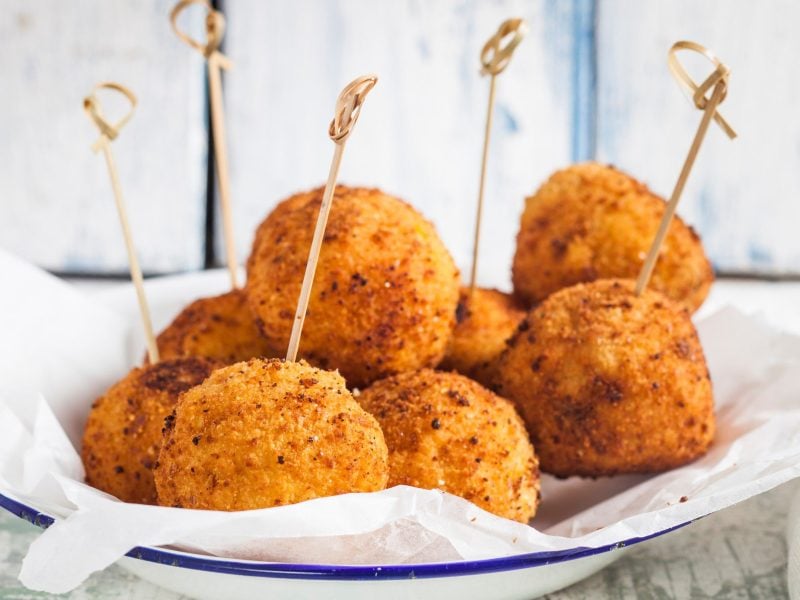 Ein Teller runde vegane Kroketten mit Spießen vor hellem Hintergrund.