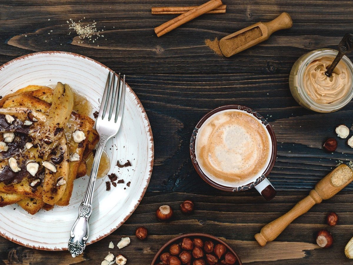 Unser veganes French Toast mit gebackenen Bananen liegt auf einem weißen Teller. Das French Toast ist angerichtet mit Schokolade und Haselnüssen.