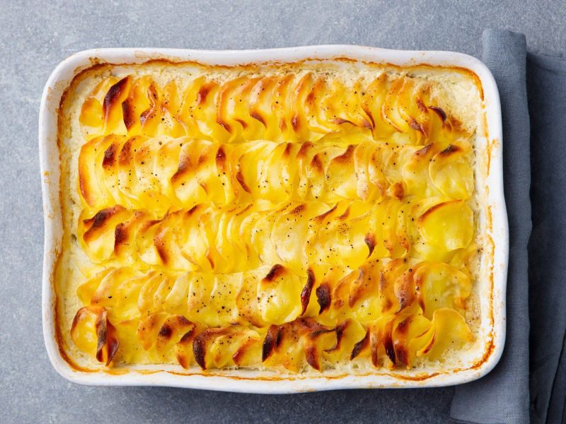 Eine weiße Auflaufform mit veganem Kartoffelgratin in der Draufsicht, daneben liegt eine Stoffserviette.