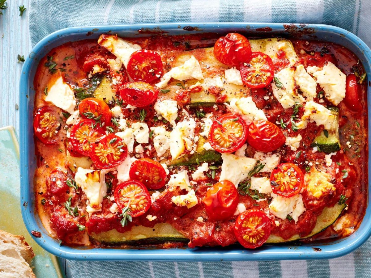 Unsere vegetarische Zucchini-Lasagne mit Tomaten steht in einer hellblauen Auflaufform auf dem Tisch.