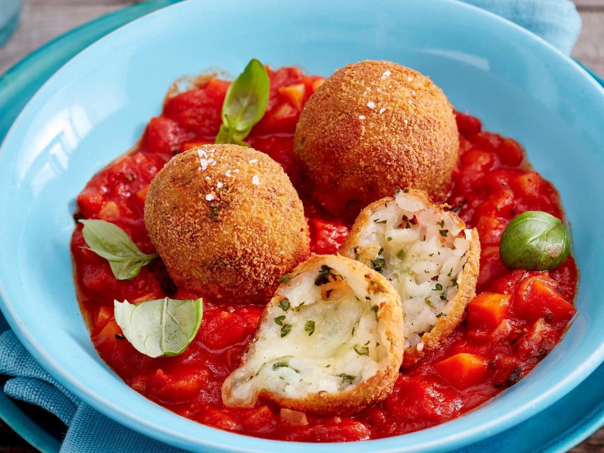 Arancini mit Tomatensugo auf einem blauen Teller. Das Ganze auf einem hölzernen Untergrund.