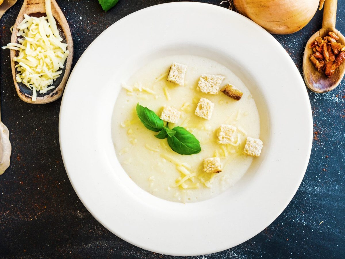 Weißer Teller mit Bergkäsesuppe und Croutons auf dunkelblauem Untergrund.