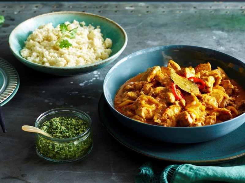 Blaue Schale gefüllt mit Chicken-Curry. Daneben befindet sich eine Schale Joghurt und eine weitere Schale Blumenkohlreis.